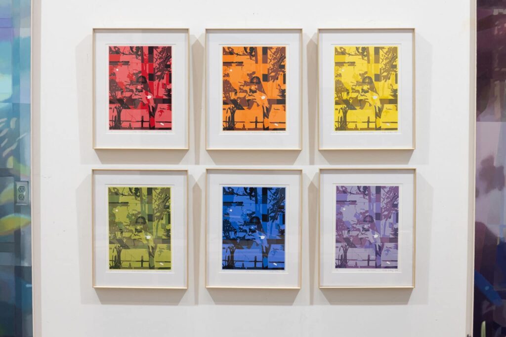 Six framed prints in shifting colours hang in a grid on a white gallery wall, each echoing the same layered image in a different hue.